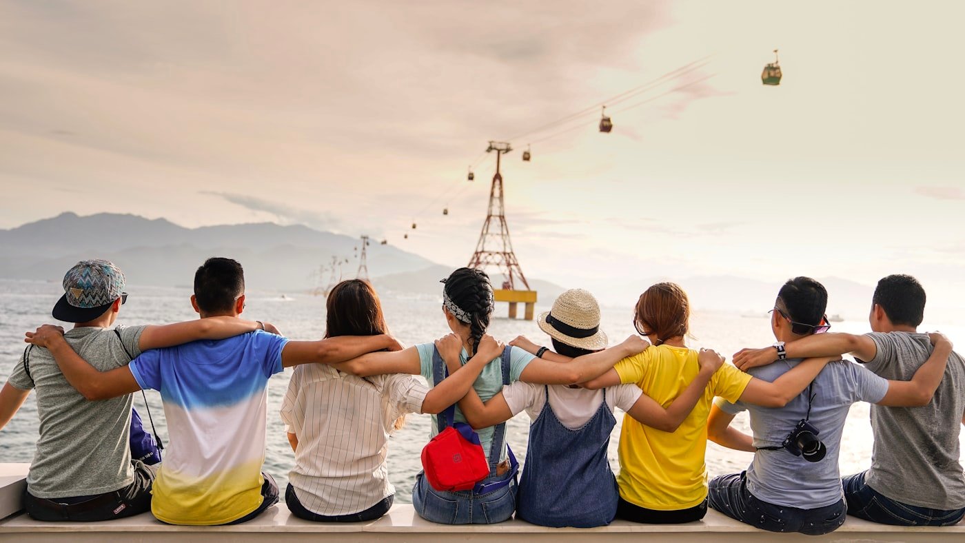 A group of young people sitting together outdoors with their arms around each other's shoulders