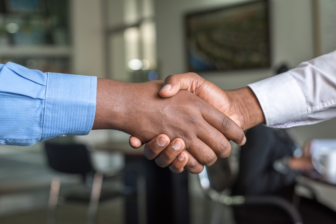Two professionals shaking hands across a meeting table to confirm a partnership